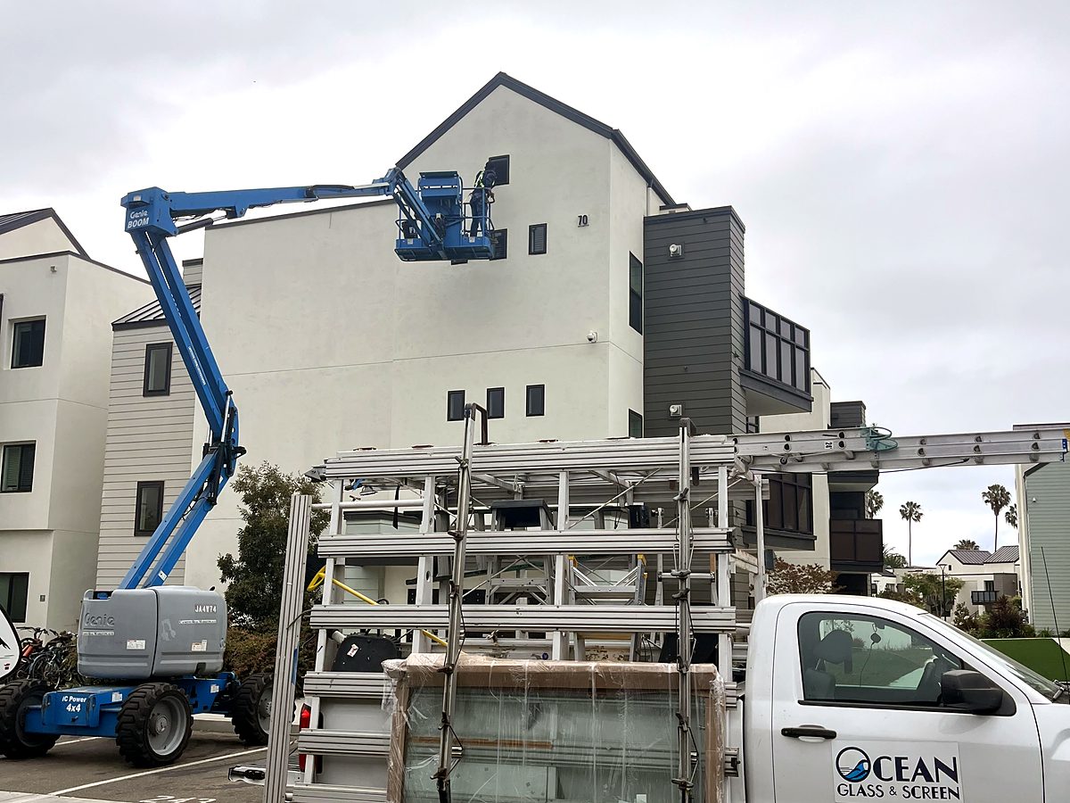 An Ocean Glass and Screen truck loaded with glass panels beside a boom lift at a job site