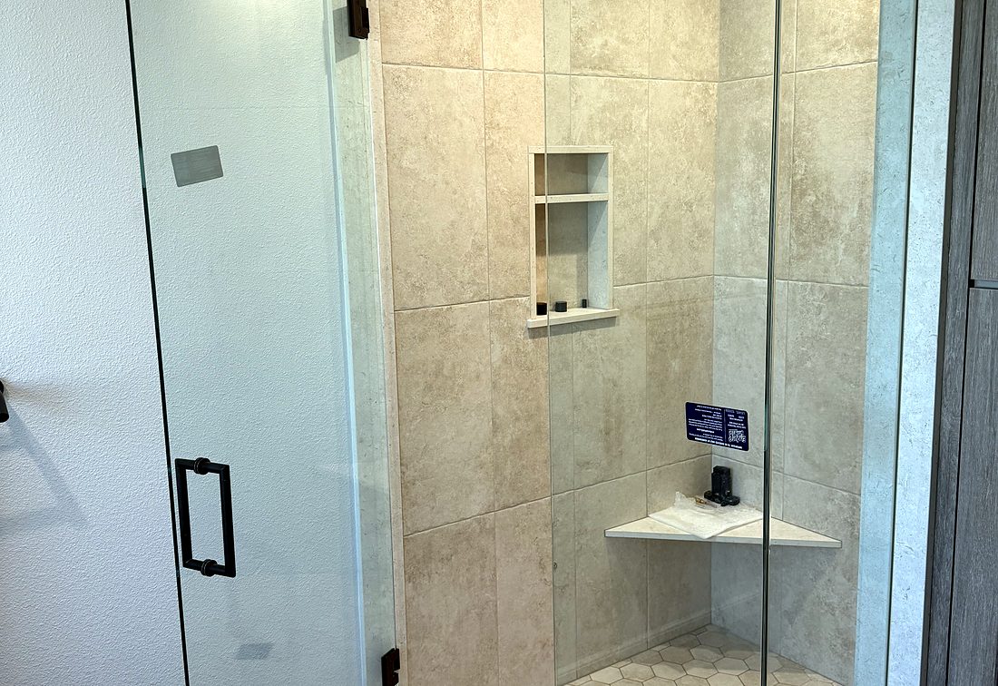 A frameless shower enclosure in travertine tile with a corner bench and matte black hardware