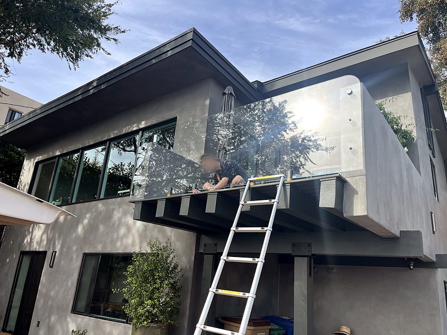 An Ocean Glass technician on a ladder fitting a frameless glass balcony railing