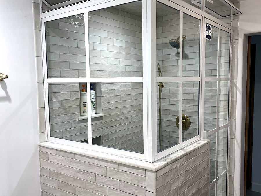 A framed glass shower enclosure with a transom, marble sill and brass fittings