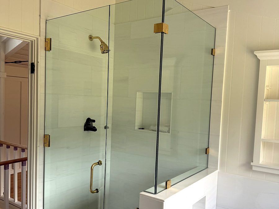 A frameless glass shower enclosure with brass hardware beside a freestanding tub