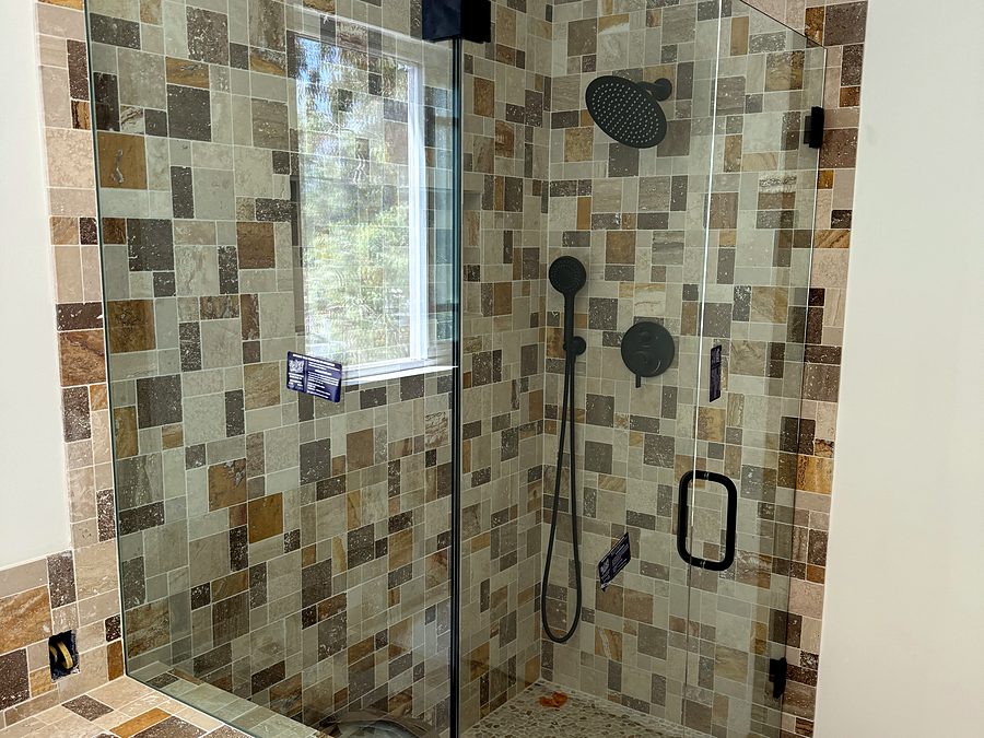 A frameless shower enclosure in multicoloured mosaic tile with black fixtures