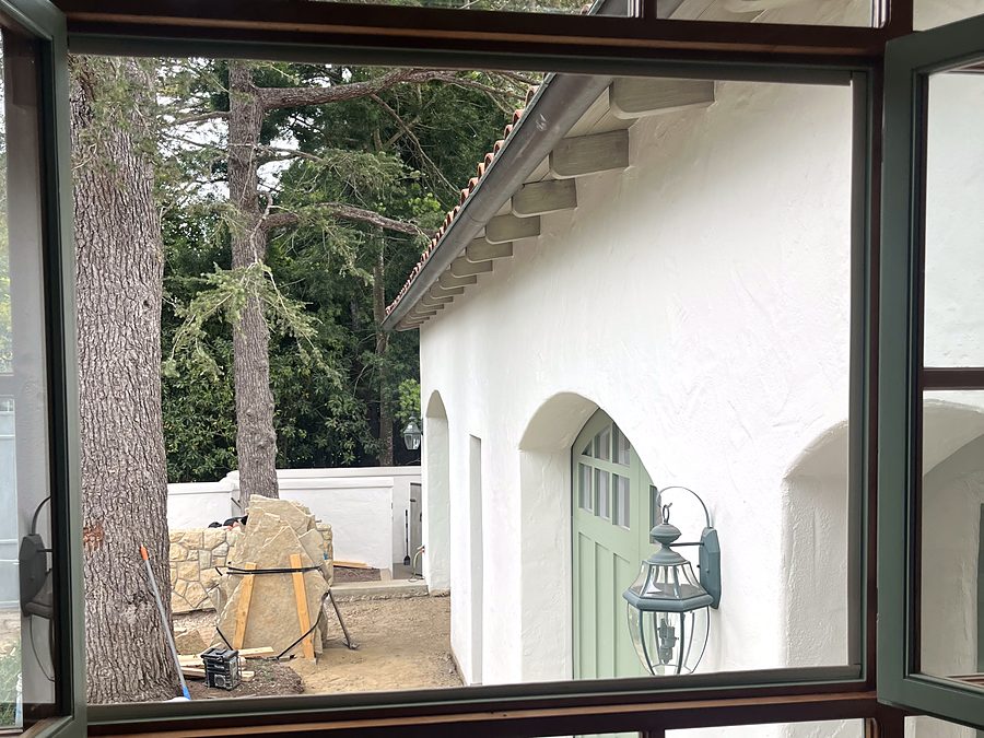 A large wood framed window looking out onto a Spanish style courtyard